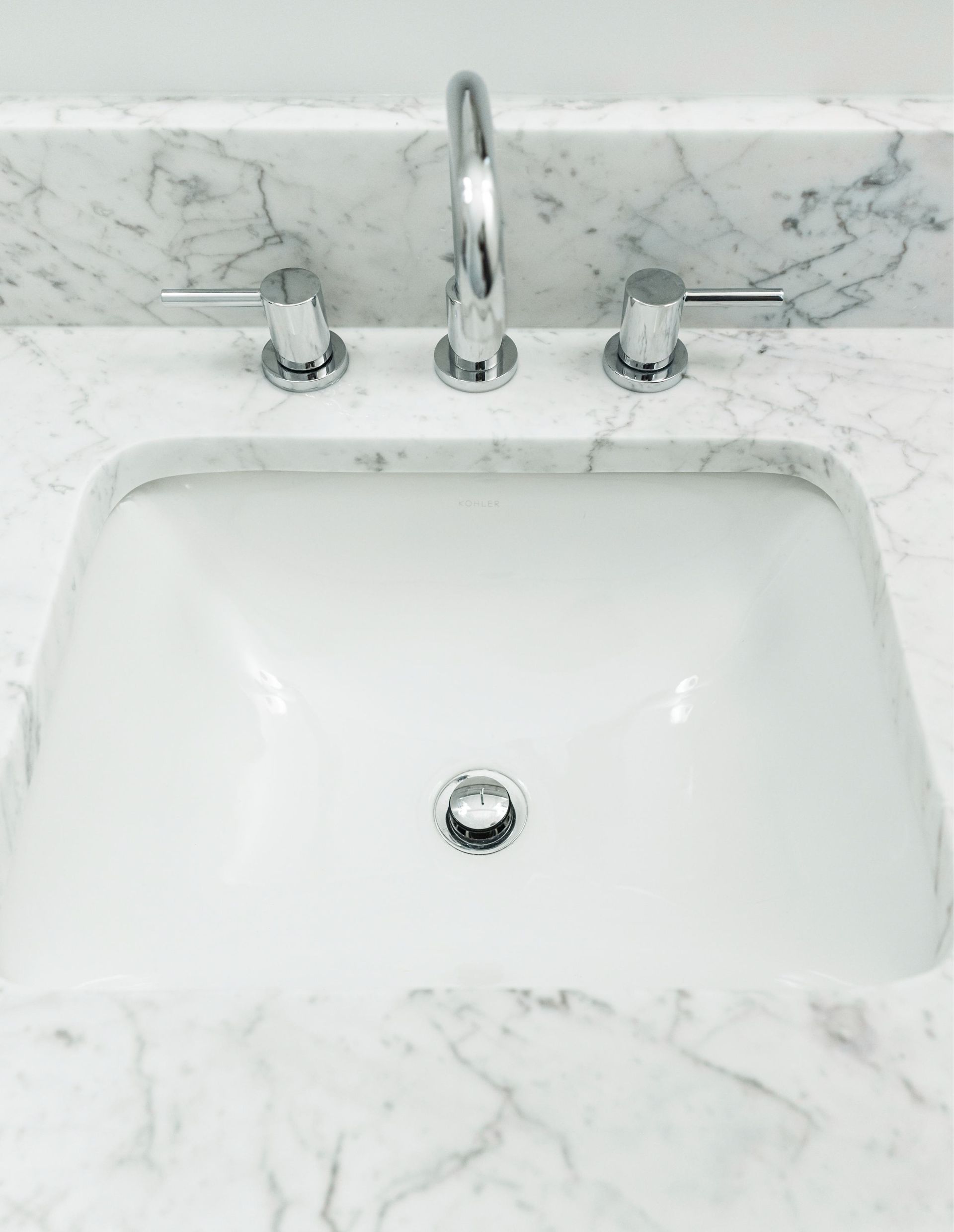 White marble bathroom sink with chrome faucet and knobs under a matching backsplash.