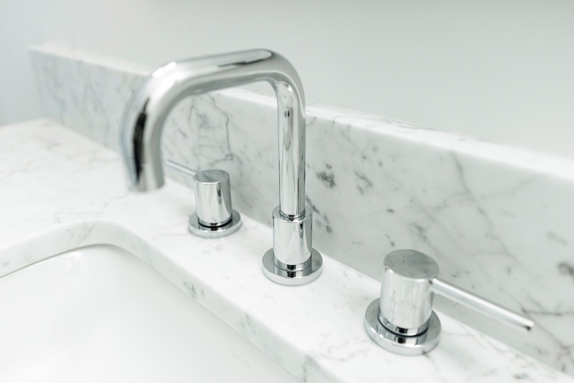 Chrome bathroom faucet with two knobs on a white marble sink countertop