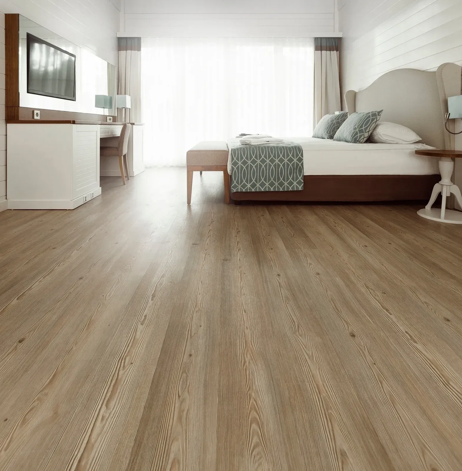 Bedroom with light brown hardwood floor, white walls, and a bed with blue accent pillows.