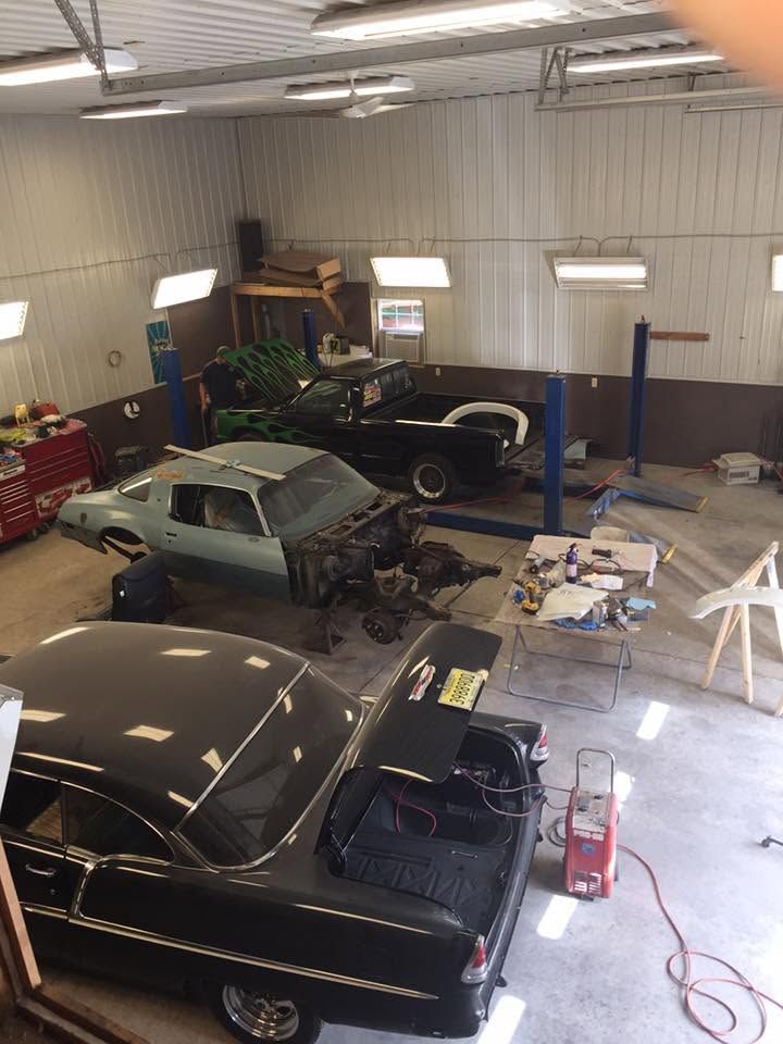 Classic cars in a garage workshop with tools, parts, and a lift, seen from above