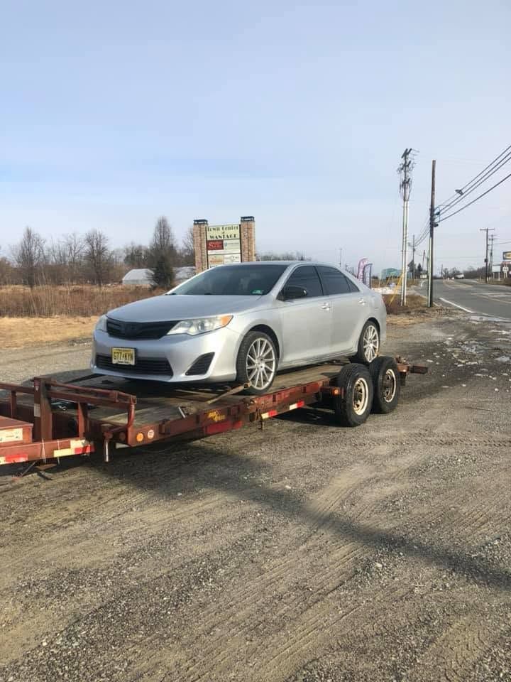 Silver sedan loaded on a red flatbed trailer on a gravel roadside under a clear sky.