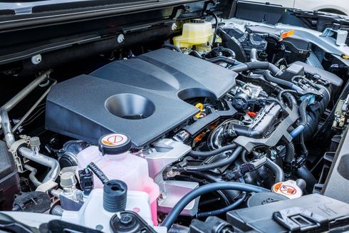 Car engine bay with black cover, pink coolant reservoir, and visible hoses and components