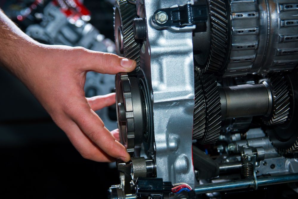 Hand inspecting a car engine component with metal gears and belts visible