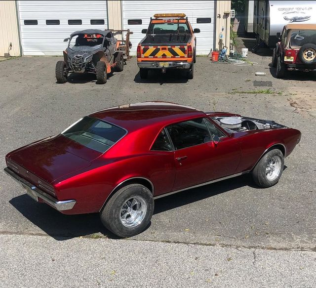 Maroon classic muscle car parked on gravel lot near tow trucks and garage doors