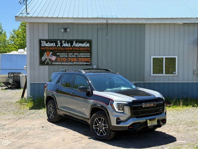 Gray GMC SUV parked in front of a gray auto body shop with a sign
