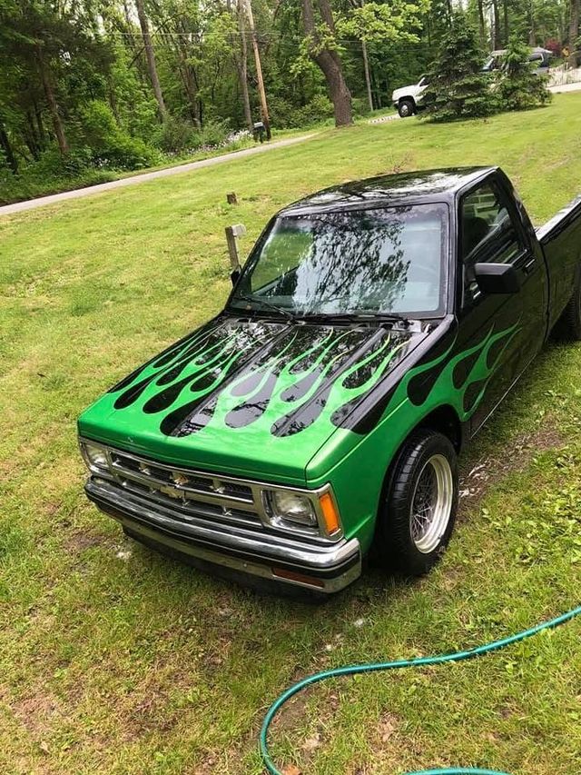 Green and black customized pickup truck parked on a grassy lawn with trees in the background