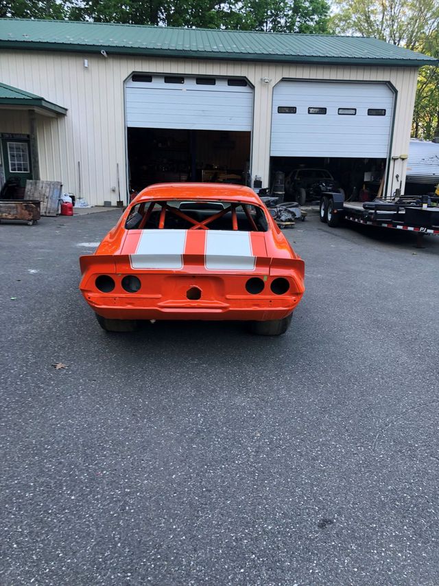 Orange classic car with white racing stripes parked in front of a garage