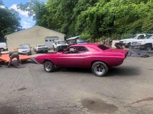 Bright pink classic muscle car parked on a gravel lot near a white tent and other vehicles