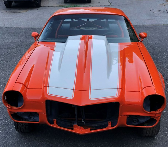 Orange classic muscle car with white racing stripes, front view, parked outdoors