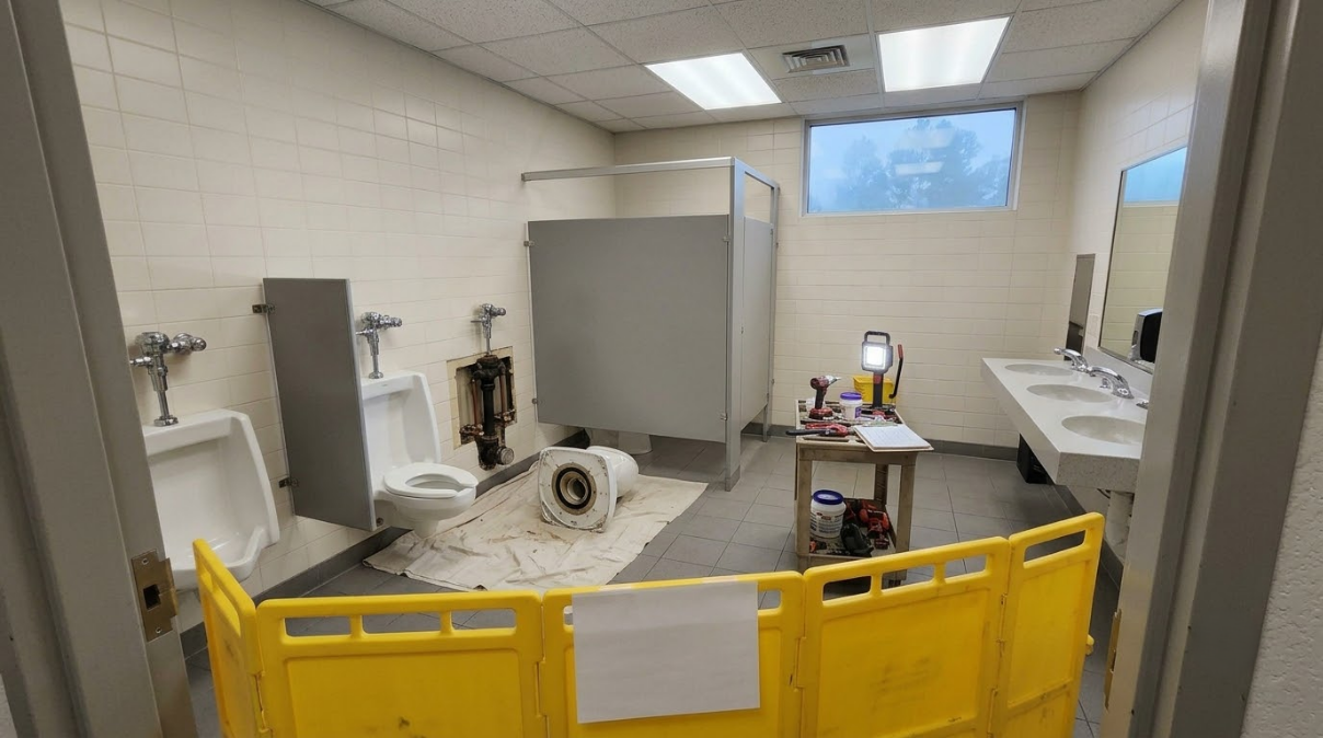 Small room with a yellow safety barrier, medical equipment, and a robot arm near a window.