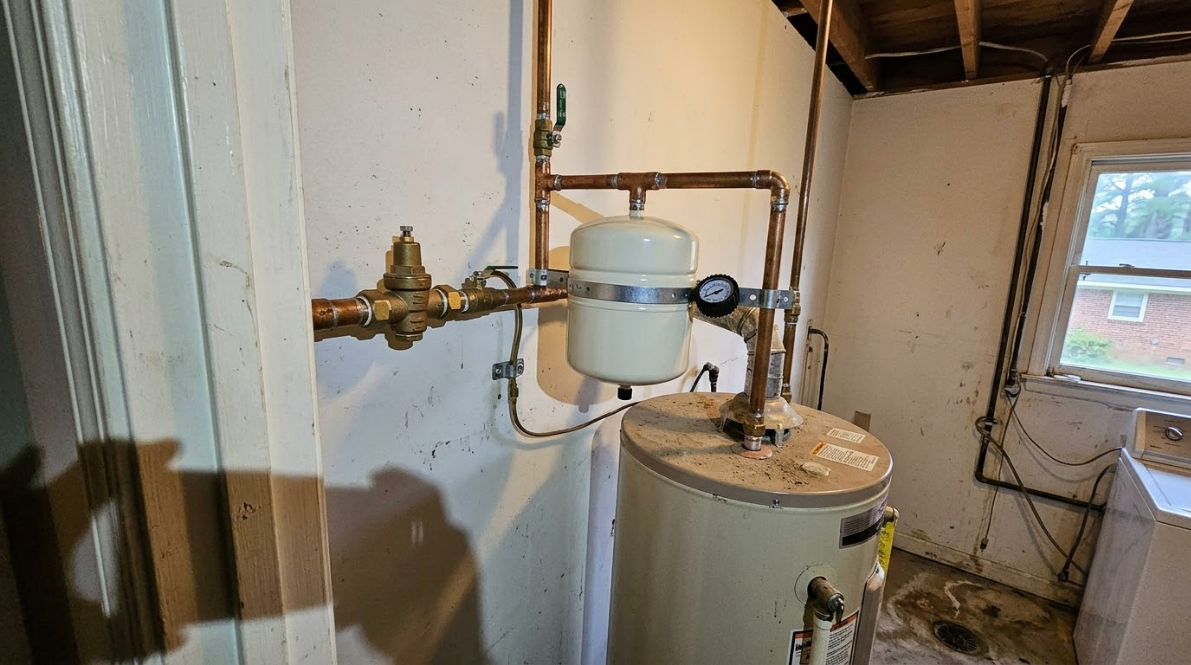 Small utility room with pipes, a pressure tank, and a water heater near a window.