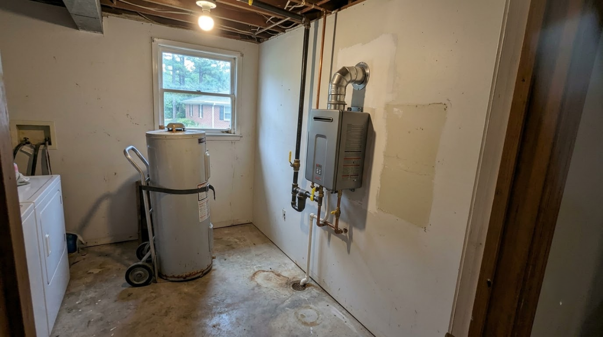 Utility room with water heater, electrical panel, exposed pipes, and a small window through the unfinished ceiling.