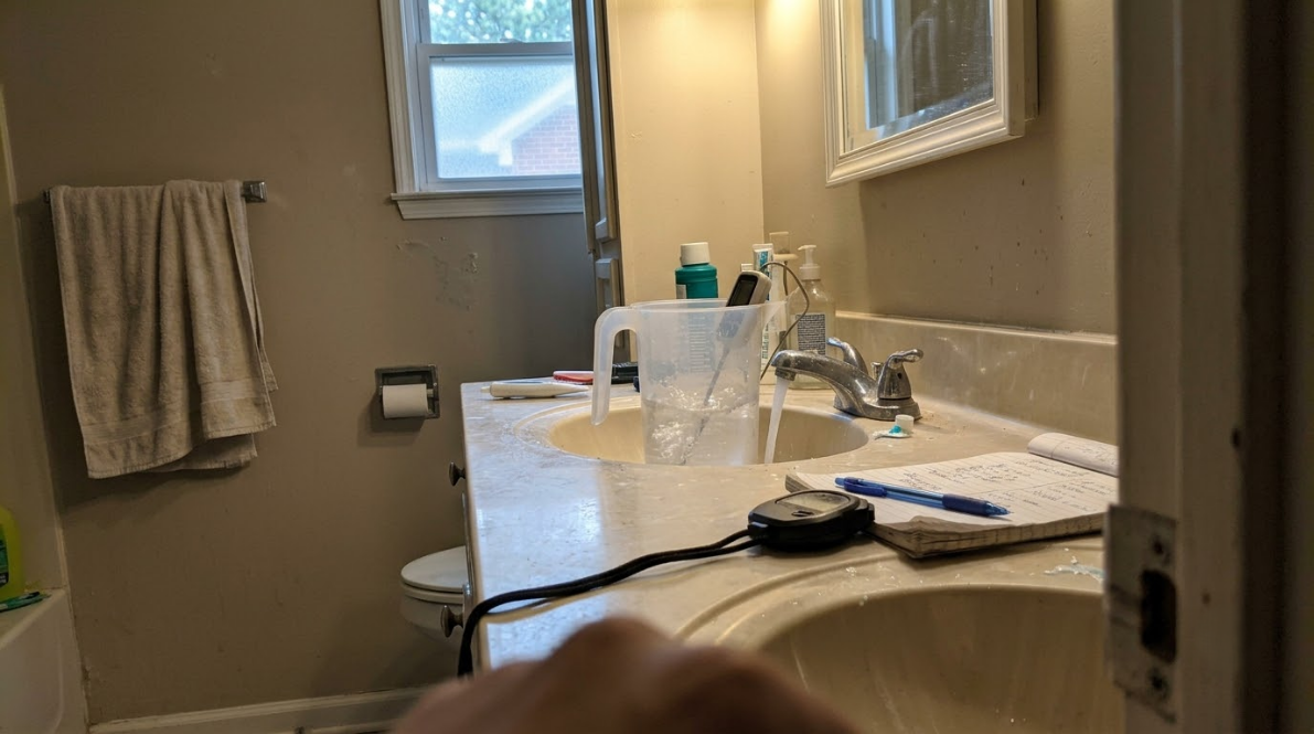 Bathroom sink and countertop with mirror, window, towel, and toiletries.