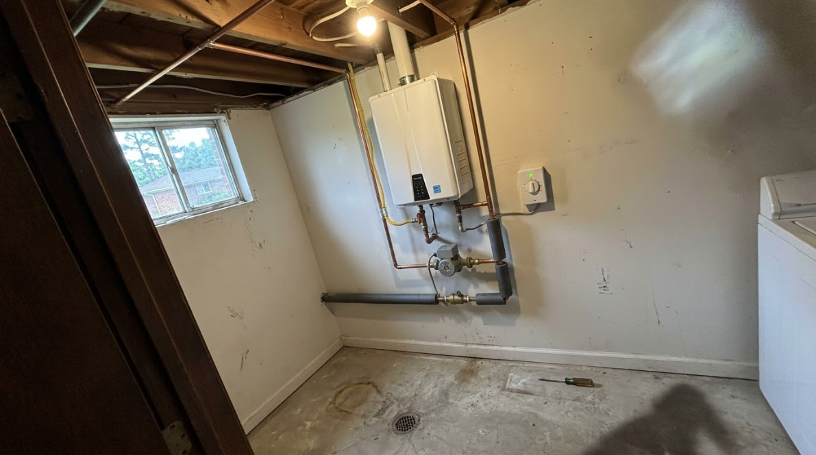 Empty basement utility room with exposed pipes, small window, and concrete floor.