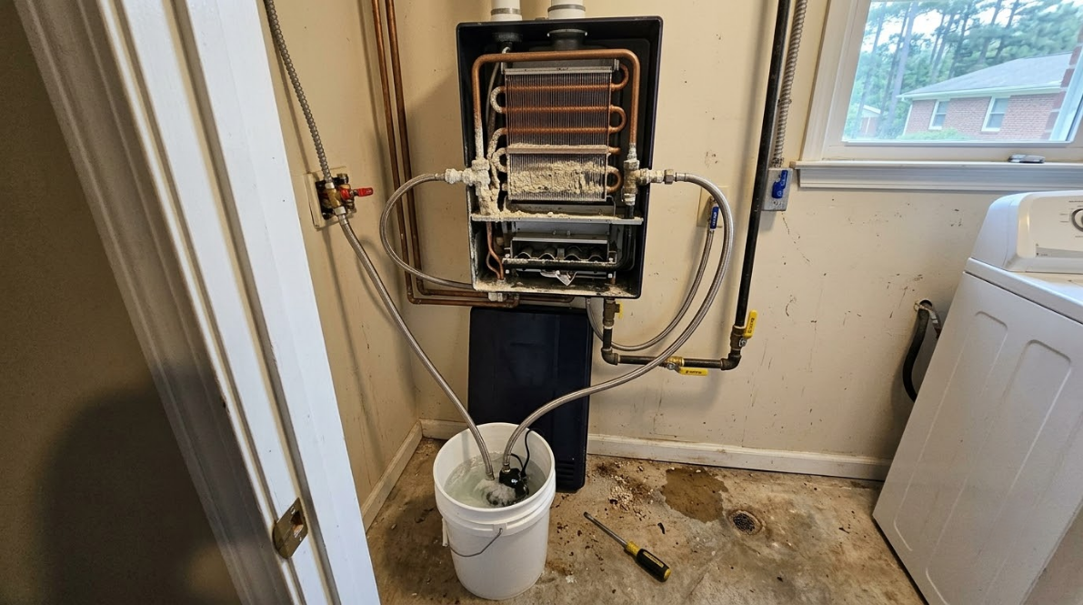 Home utility closet with exposed plumbing and pipes above a white bucket on a tiled floor