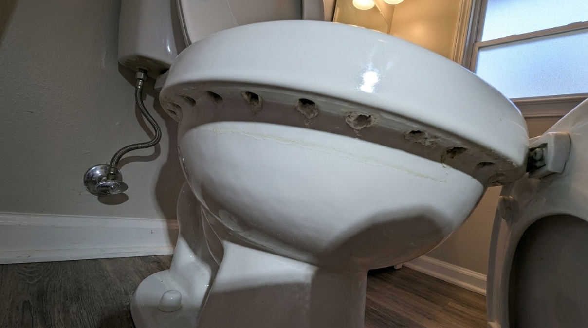 Broken white toilet with the tank detached, viewed from a low angle in a bathroom.