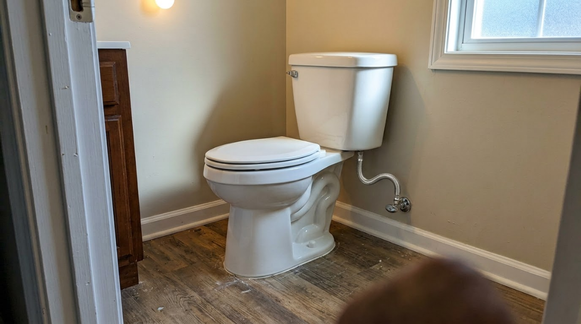 Small bathroom with a white toilet, beige walls, and wood-look flooring.