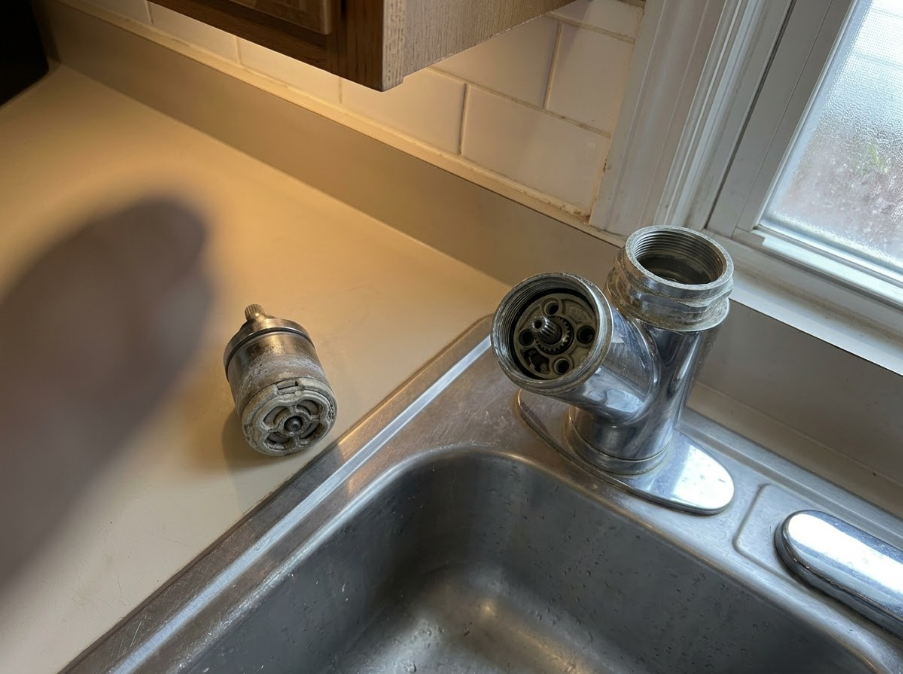 Kitchen sink with faucet parts laid out on the counter beside a window.