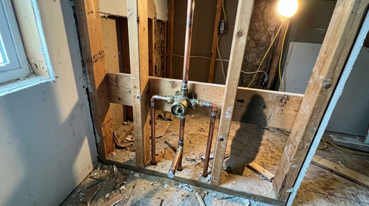 Bathroom wall studs exposed around a sink plumbing rough-in, with debris on the floor.