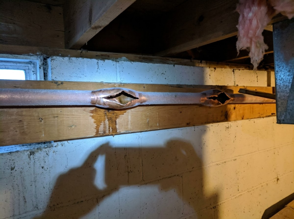 Rusty metal beam with open holes, attached to a wooden board in a basement-like space.