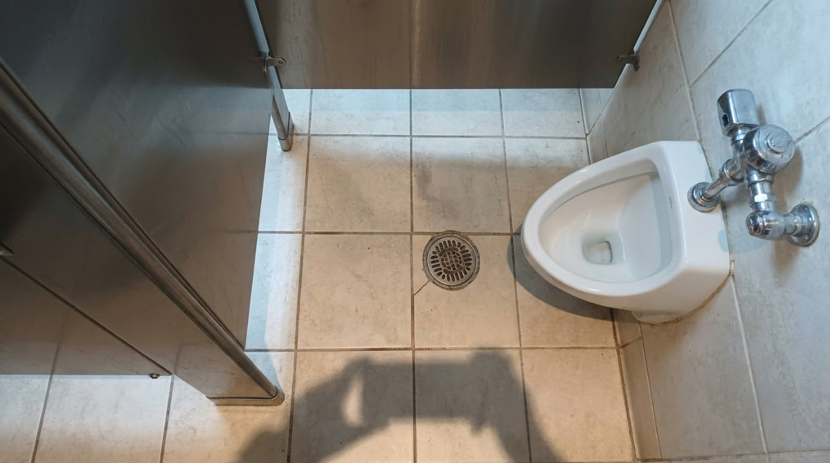 Accessible restroom with stalls, sinks, mirrors, and a cleaning cart on a tiled floor