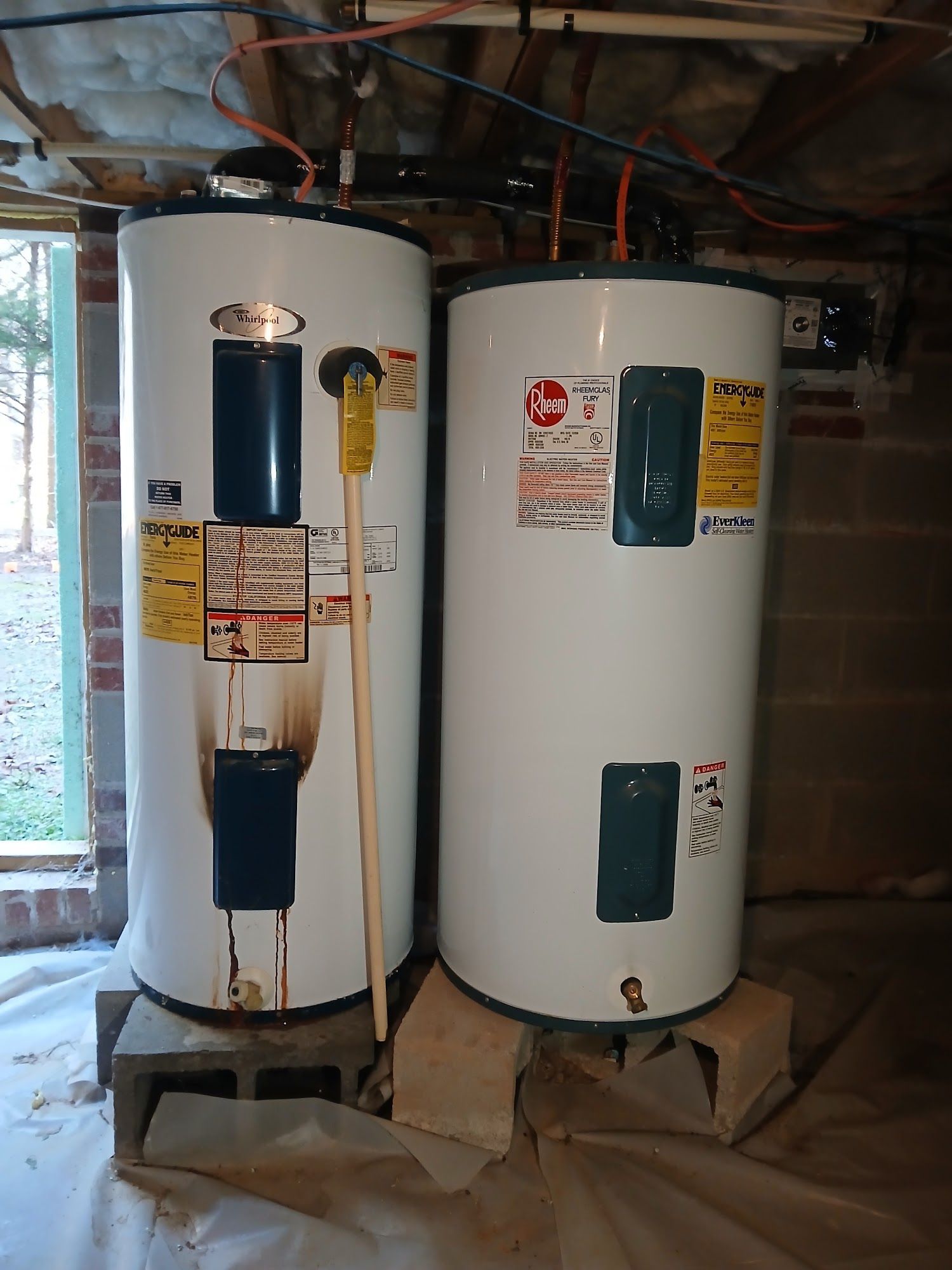 Two white water heaters in an unfinished utility room with exposed ceiling pipes.