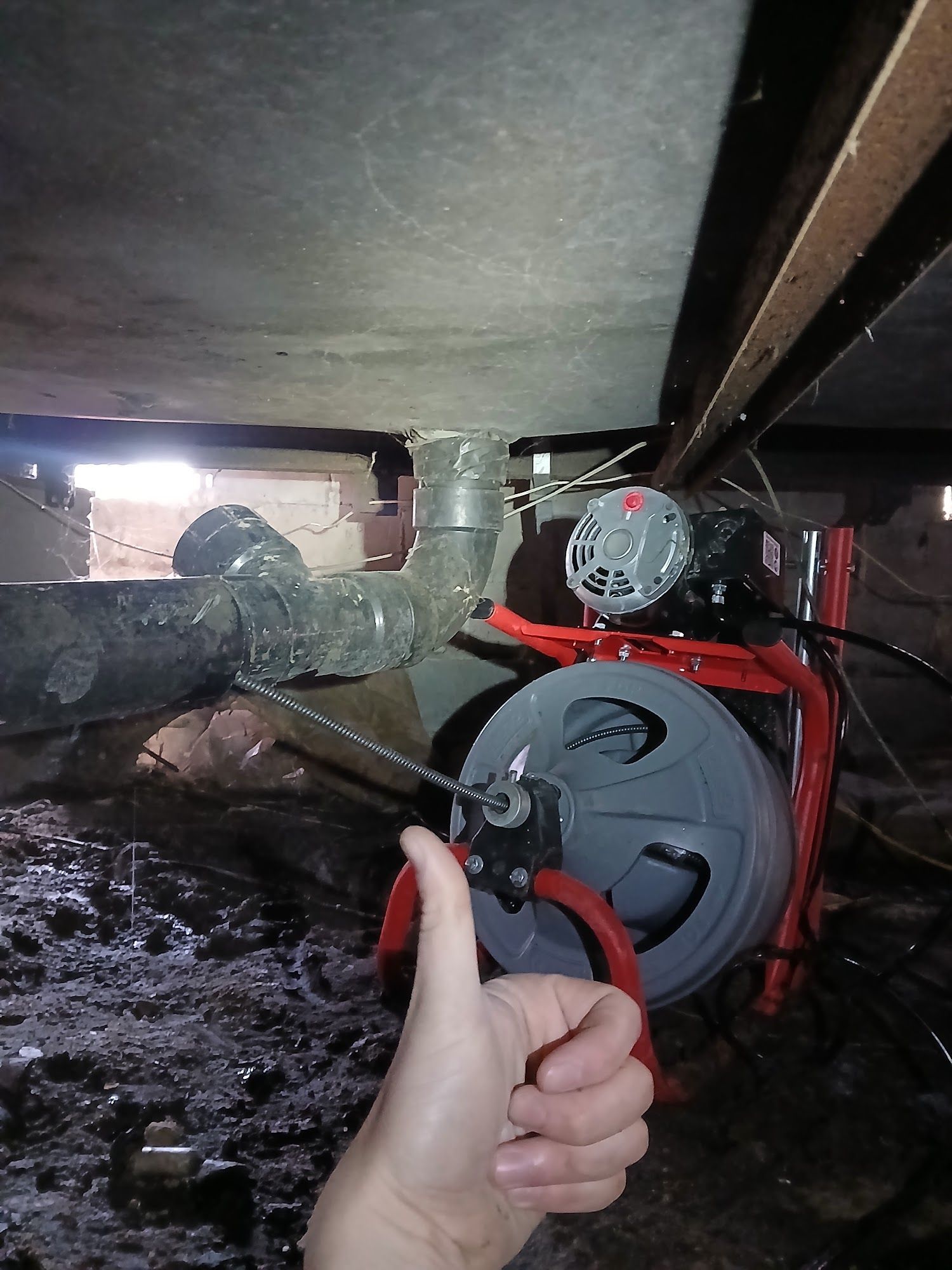 Thumbs-up in a cramped crawlspace beside a red utility pump and pipes.