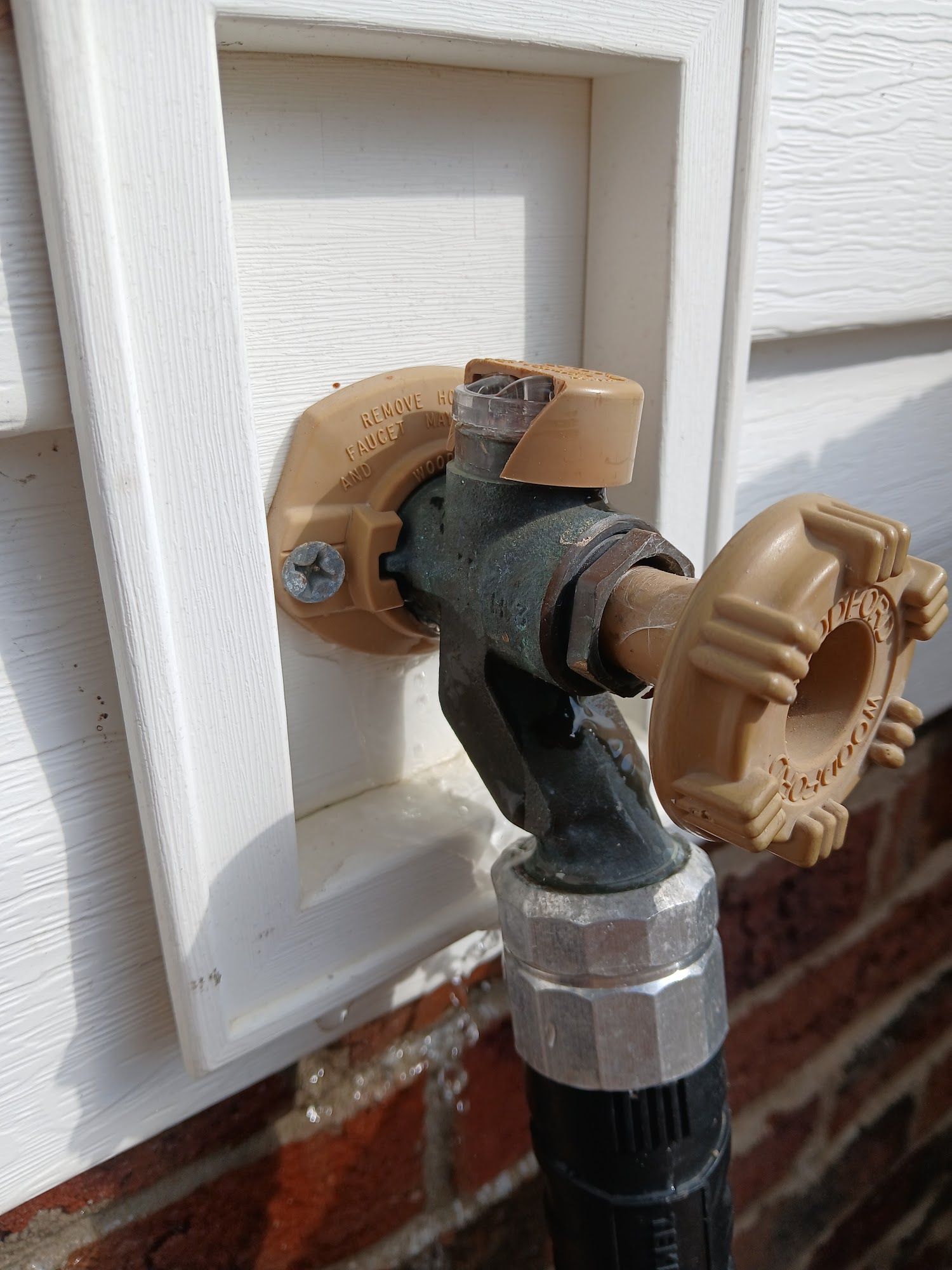 Garden hose connected to an outdoor faucet with a brass shutoff valve on a white wall