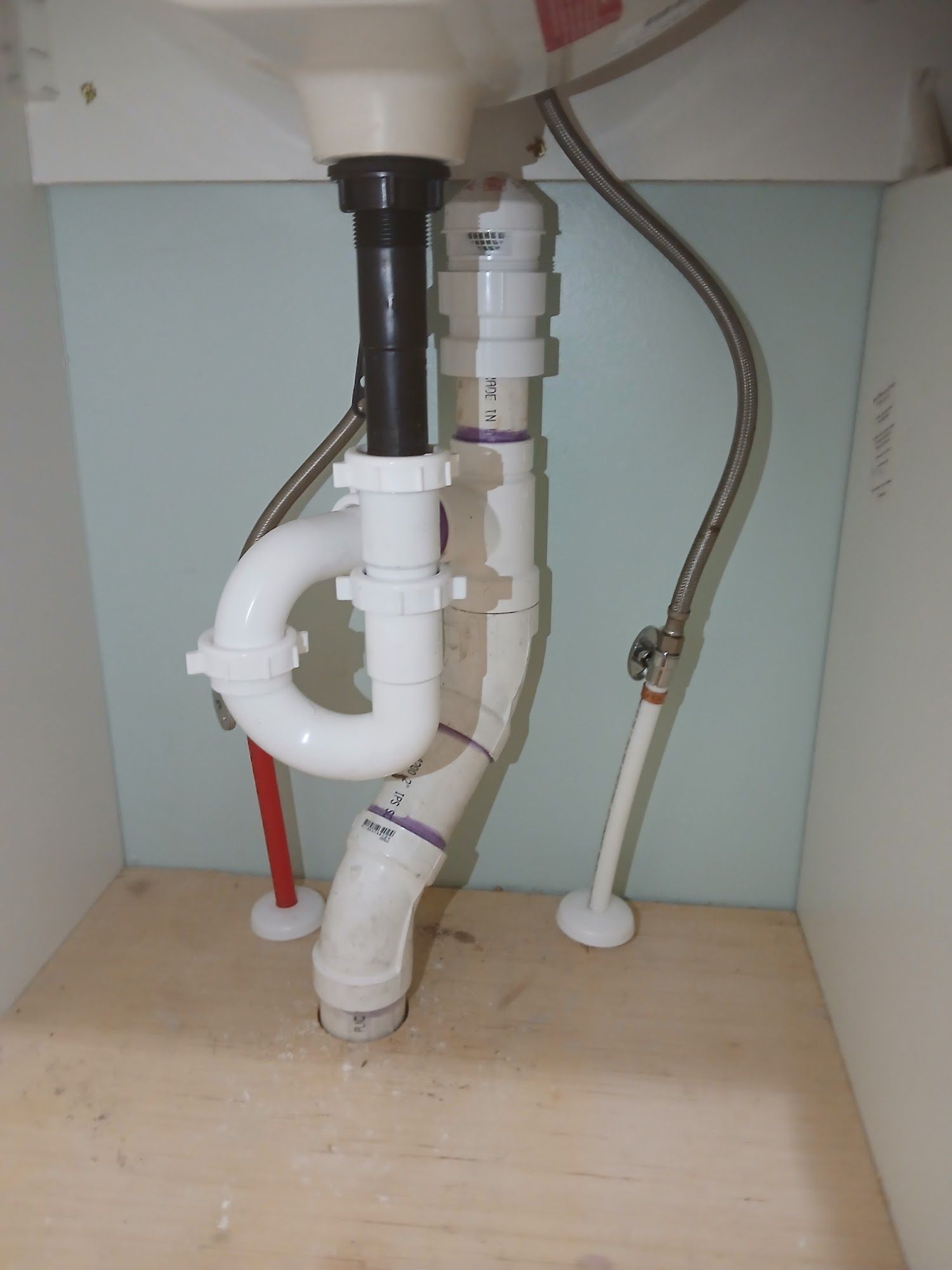 Under-sink plumbing with white PVC drain pipes and a black vertical pipe in a cabinet.