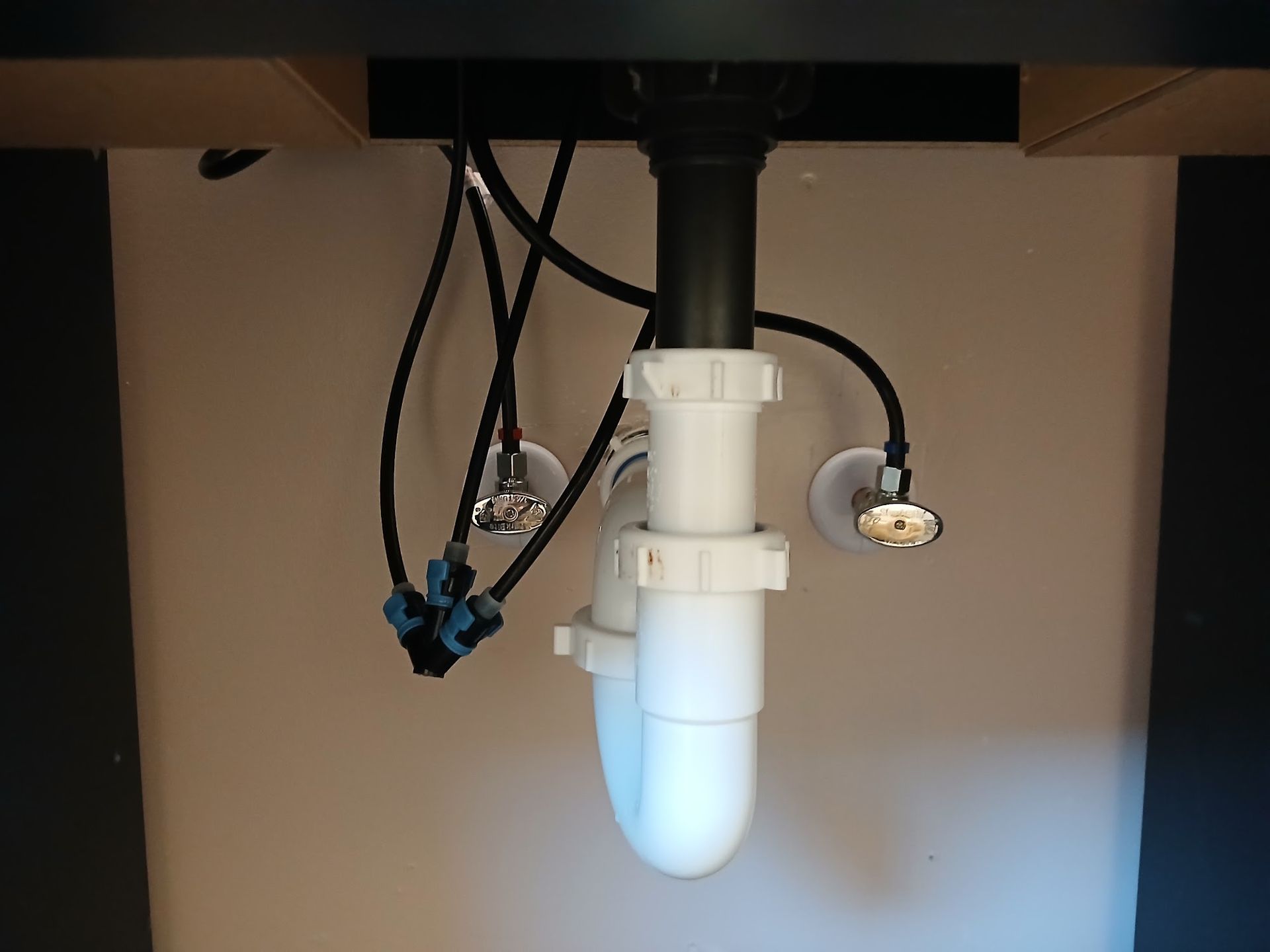 Under-sink plumbing with white PVC drain pipe and hanging wires beneath a counter