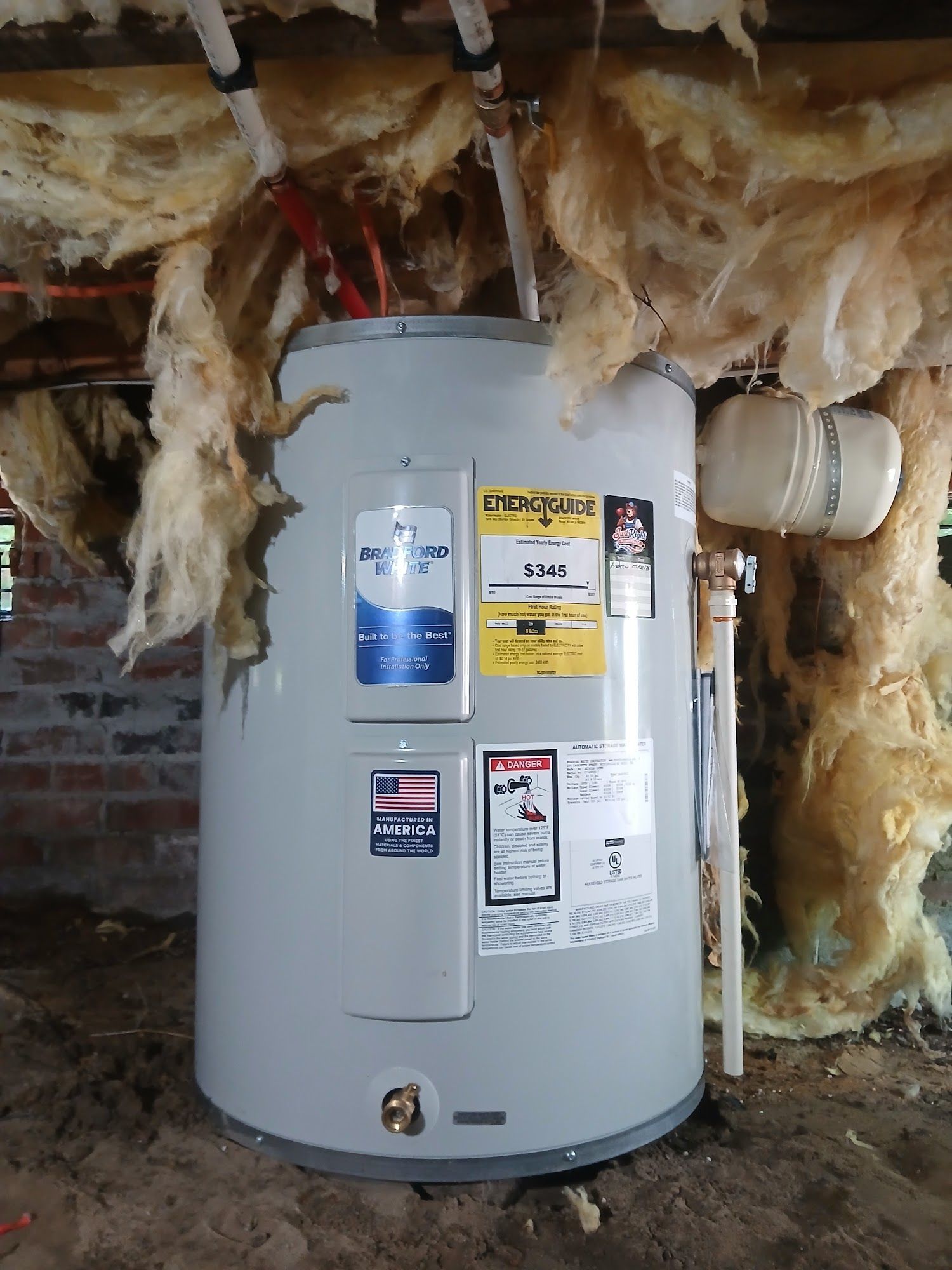 Water heater in a basement with exposed insulation and brick walls, showing several safety labels.