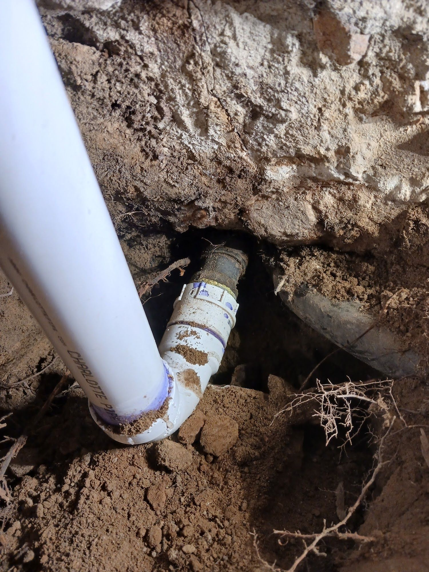 White PVC pipe connected to a cracked underground pipe in a dirt excavation hole