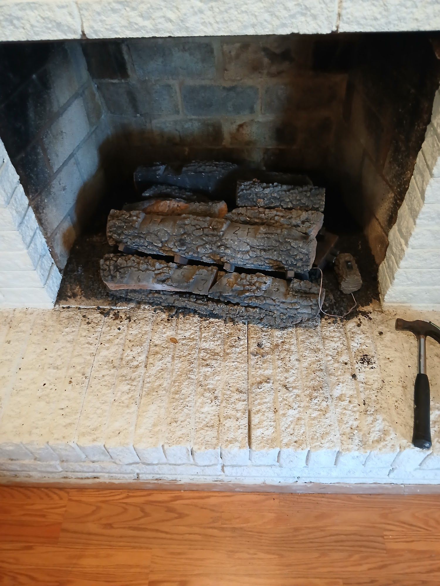 Brick fireplace with stacked logs on a hearth, framed by white trim and wood flooring.