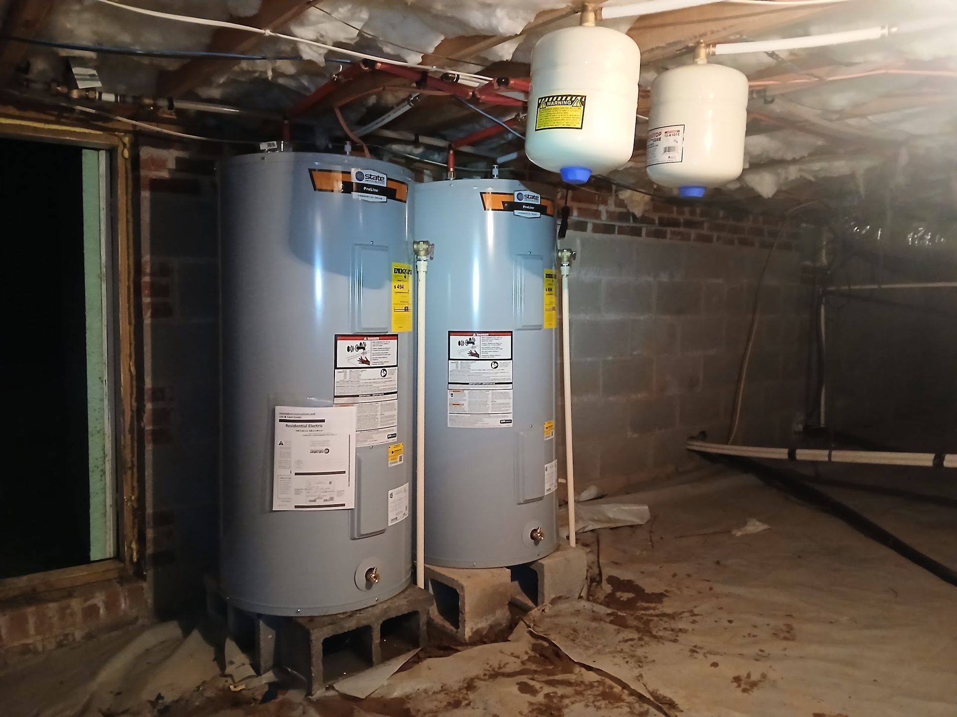 Two blue water heaters and two white expansion tanks in a basement utility room