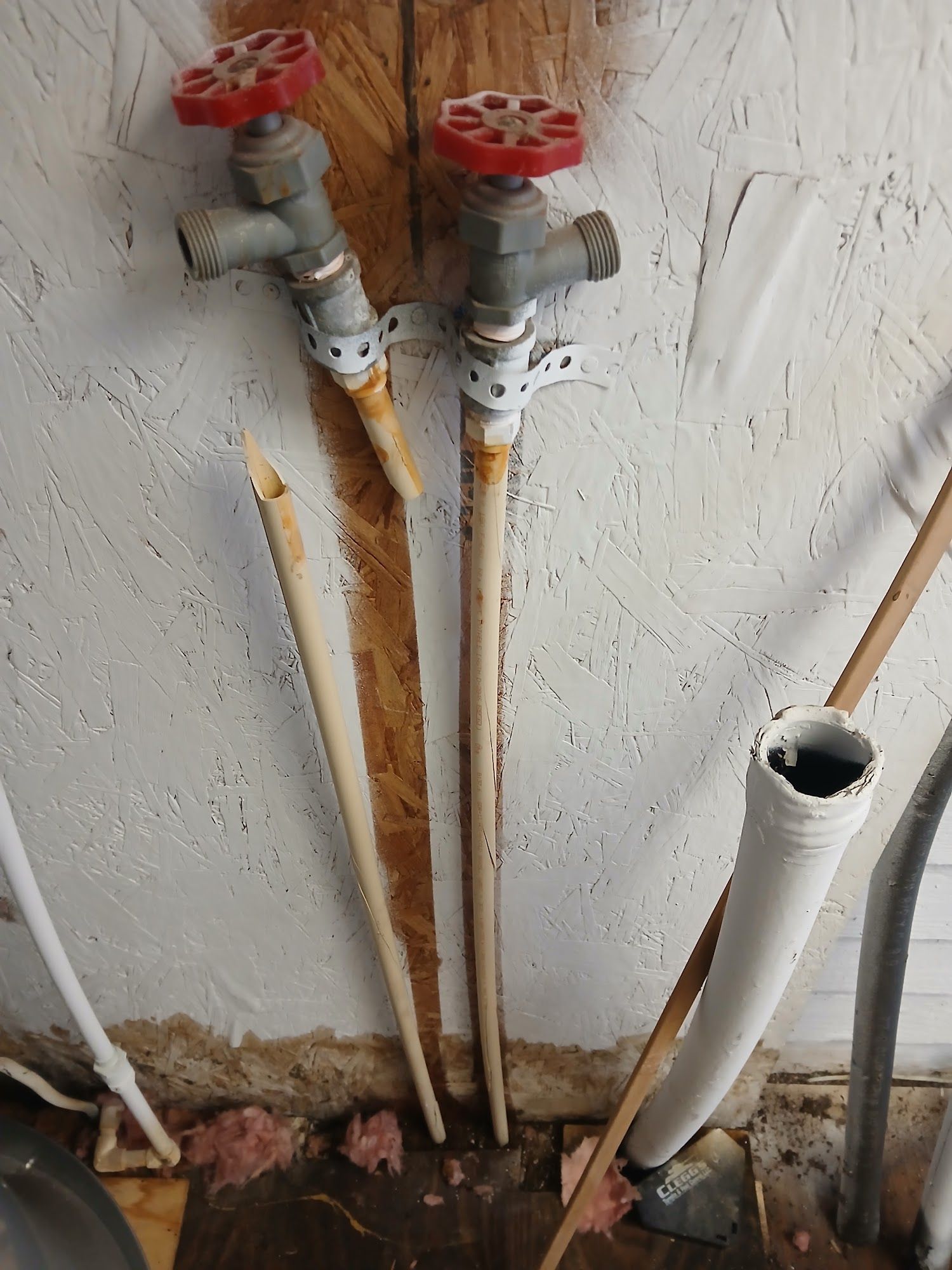 Two red valve handles on white pipes protruding from a rough wall near the floor