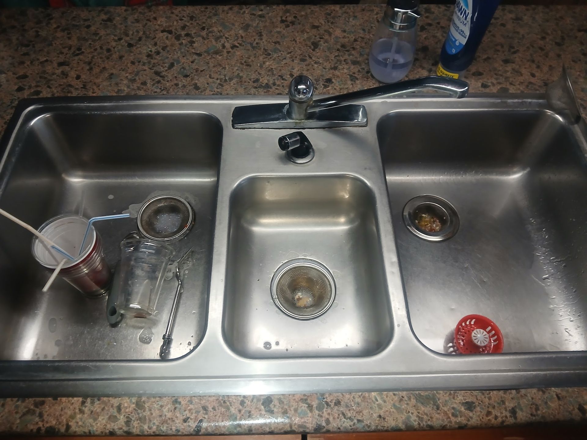 Kitchen sink with three basins, dishes and utensils in the left basin, and a red scrubber in the right basin.
