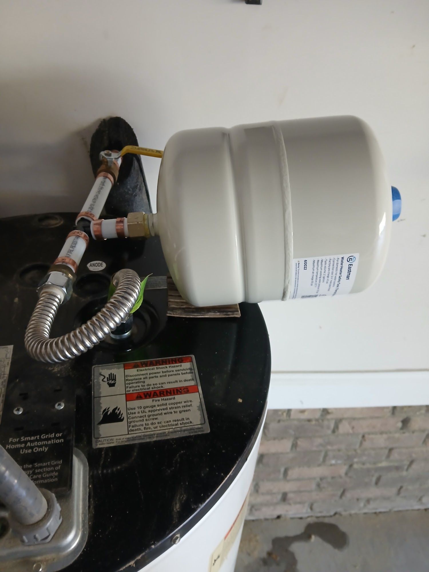 Water heater tank with pipes and a white expansion tank in a utility room