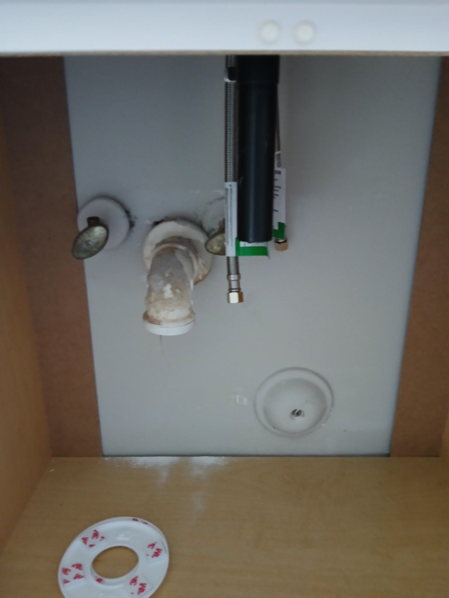 Under-sink plumbing with pipes, valves, and a small round device on the cabinet floor.