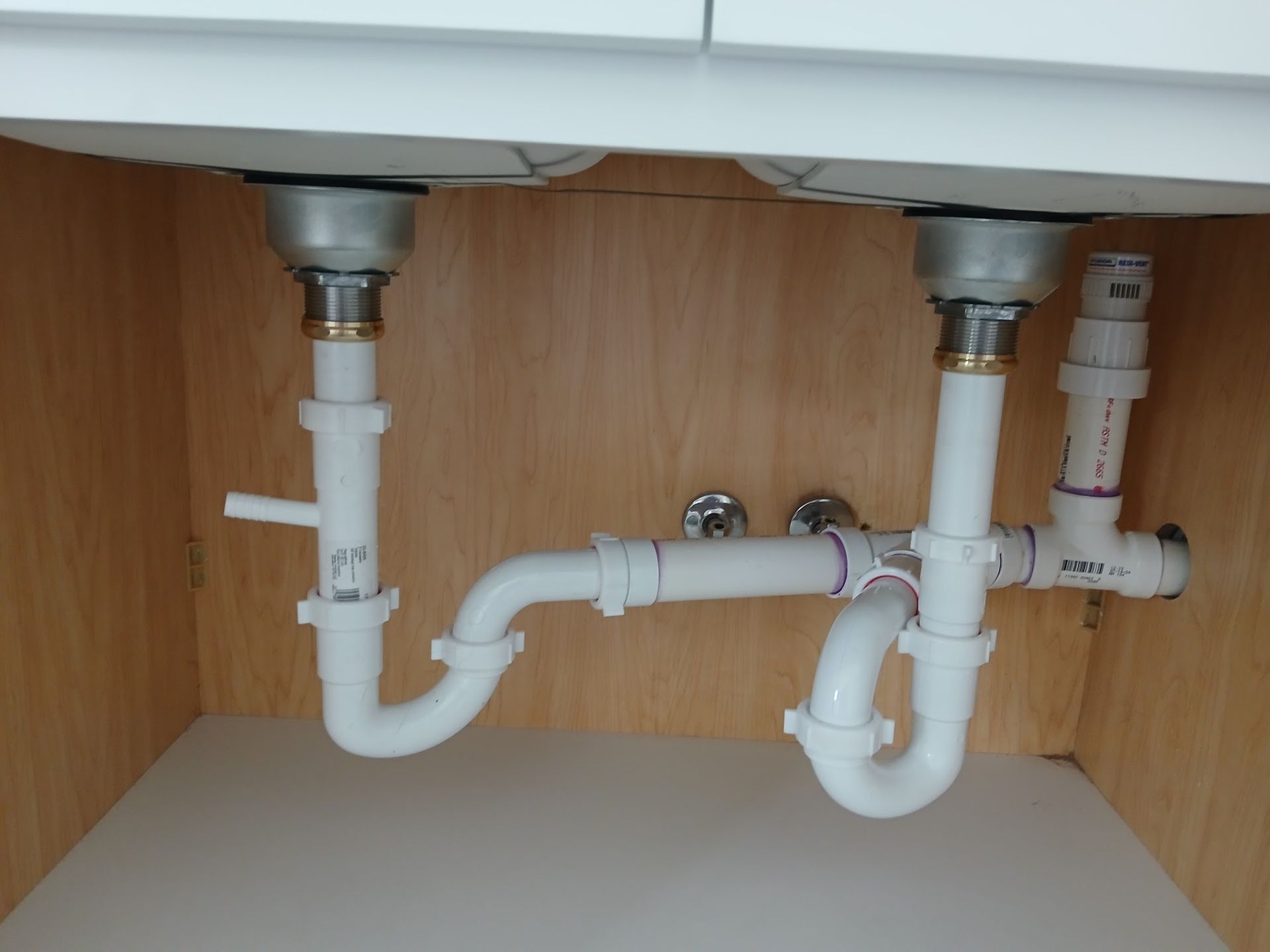 Under-sink plumbing with white drain pipes and a cabinet interior