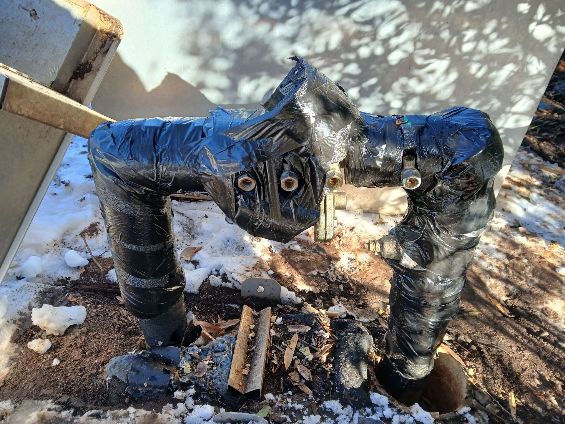 Black pipe assembly with blue tape and two circular fittings in a snowy outdoor area