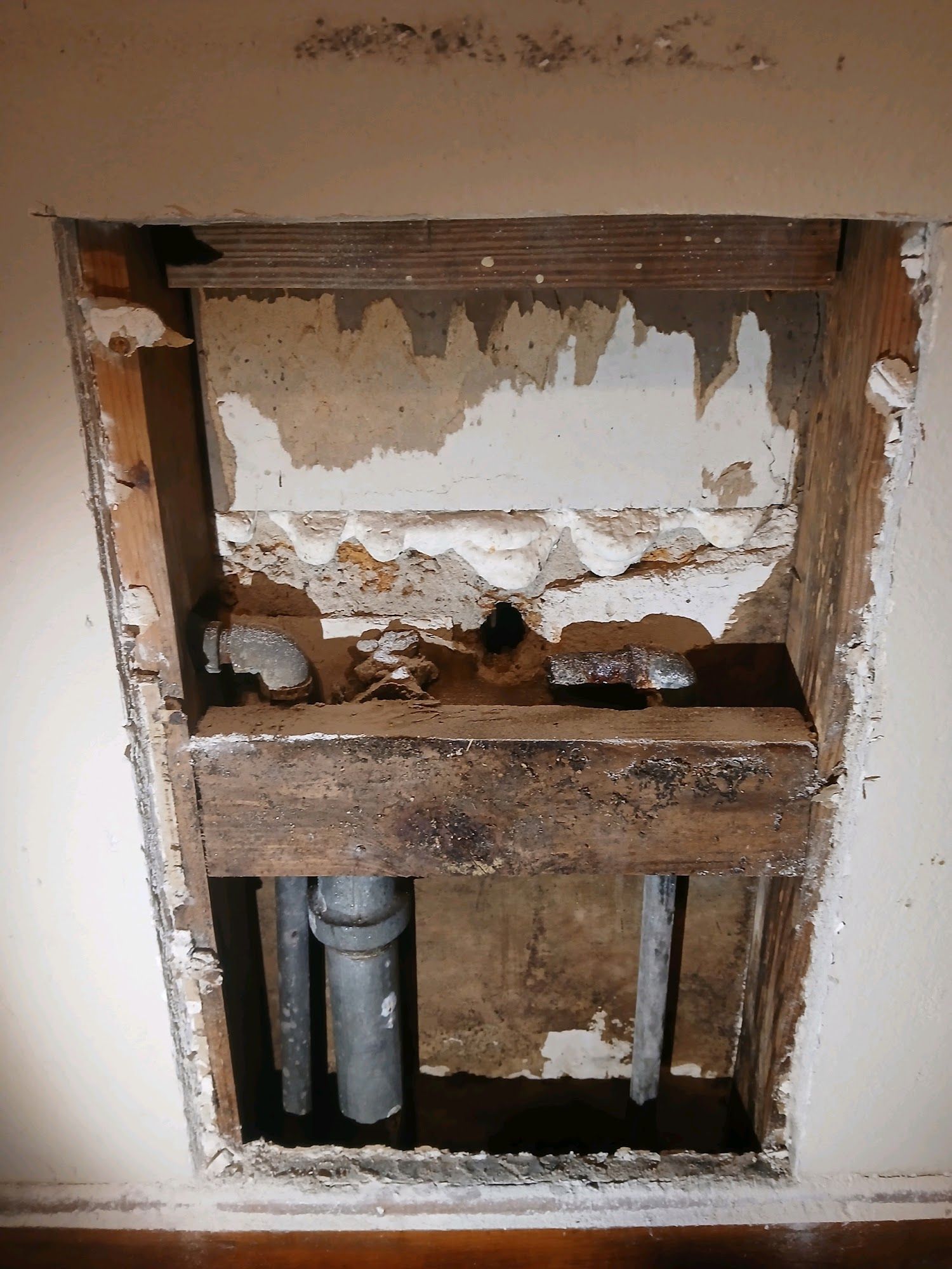 Damaged wall opening exposing pipes and torn drywall inside a home