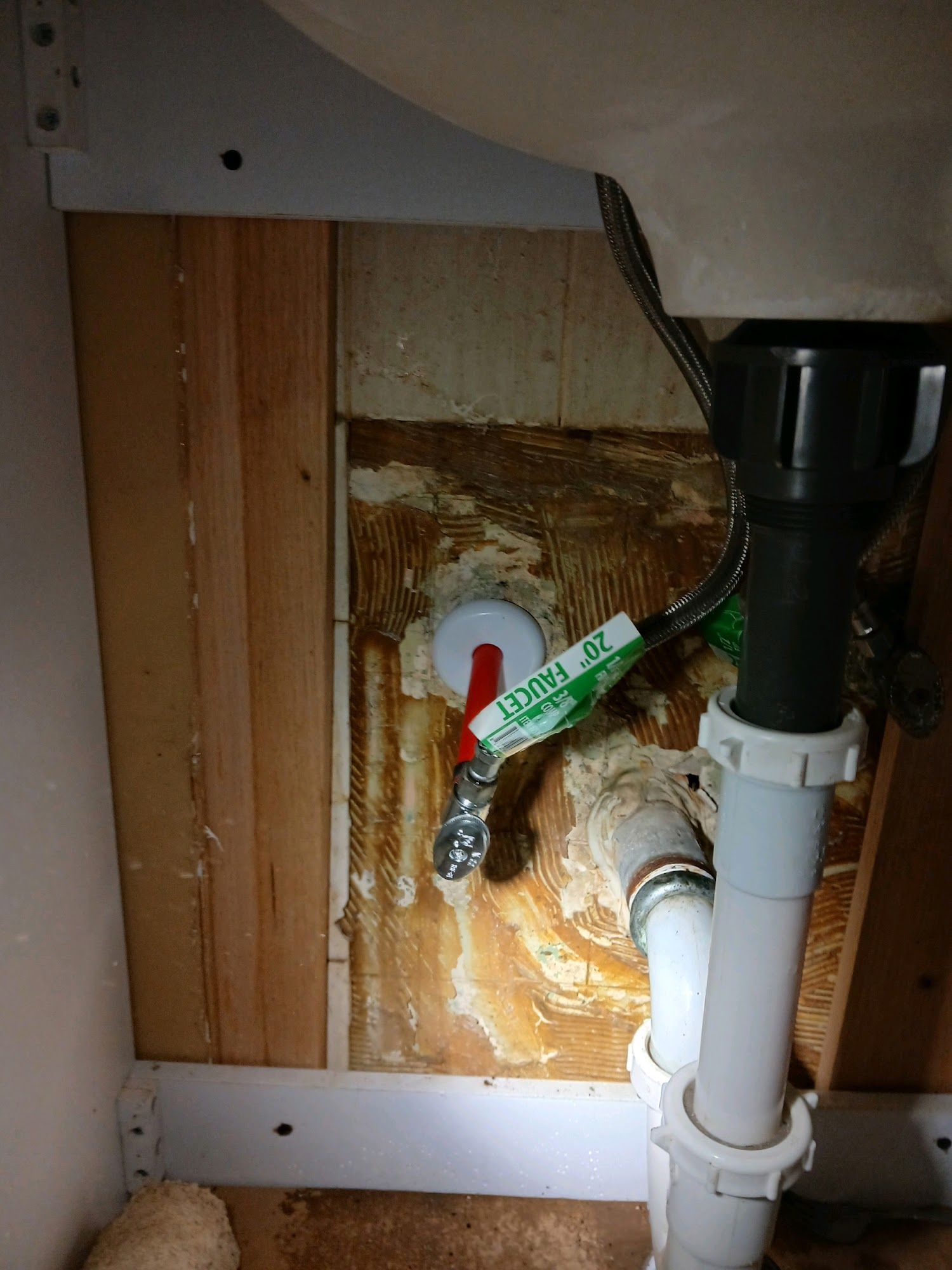Under-sink plumbing with a leaking pipe and water damage on the cabinet wall