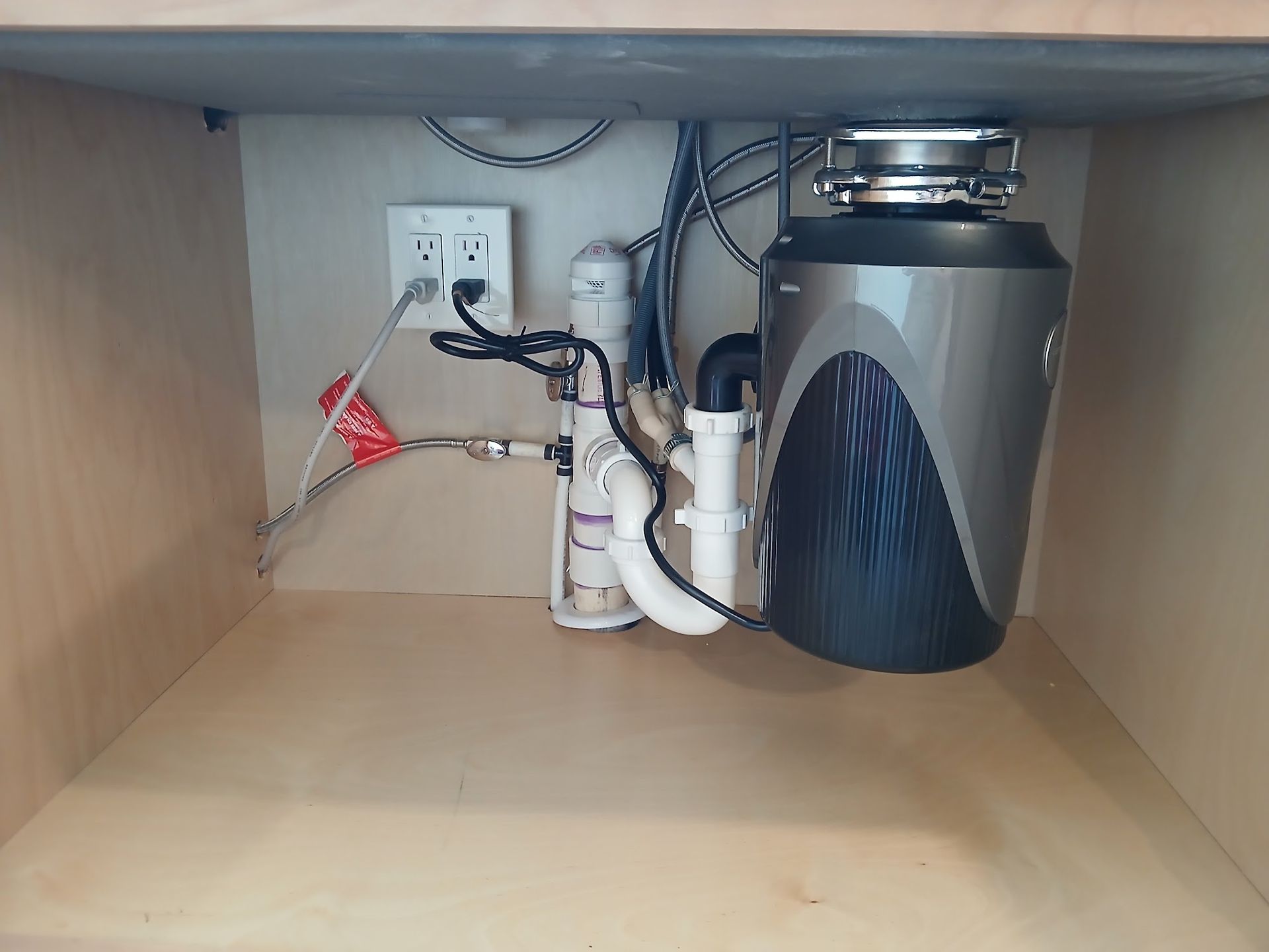 Under-sink cabinet with plumbing, shutoff valve, and a gray trash compactor or appliance on the right