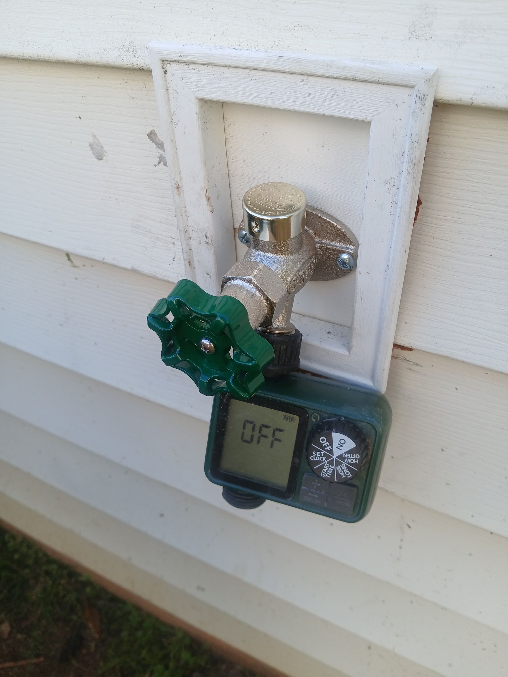 Outdoor water spigot with green handle mounted on a brick house wall near the ground