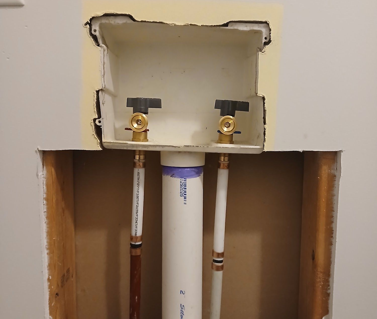 Open wall plumbing access with two shutoff valves above a white pipe and exposed framing.