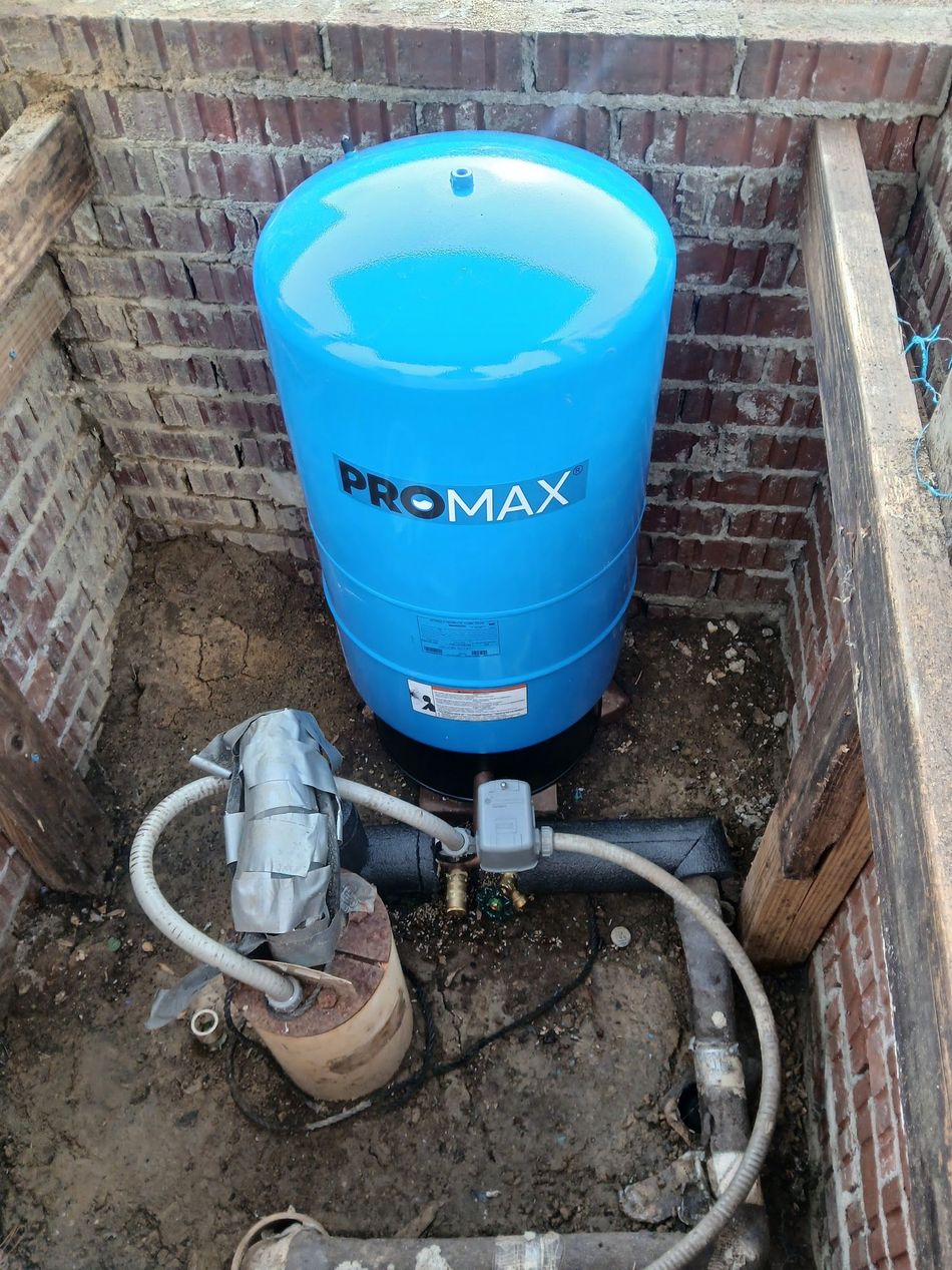 Blue PROMAX water pressure tank and pump installed in a brick utility corner.
