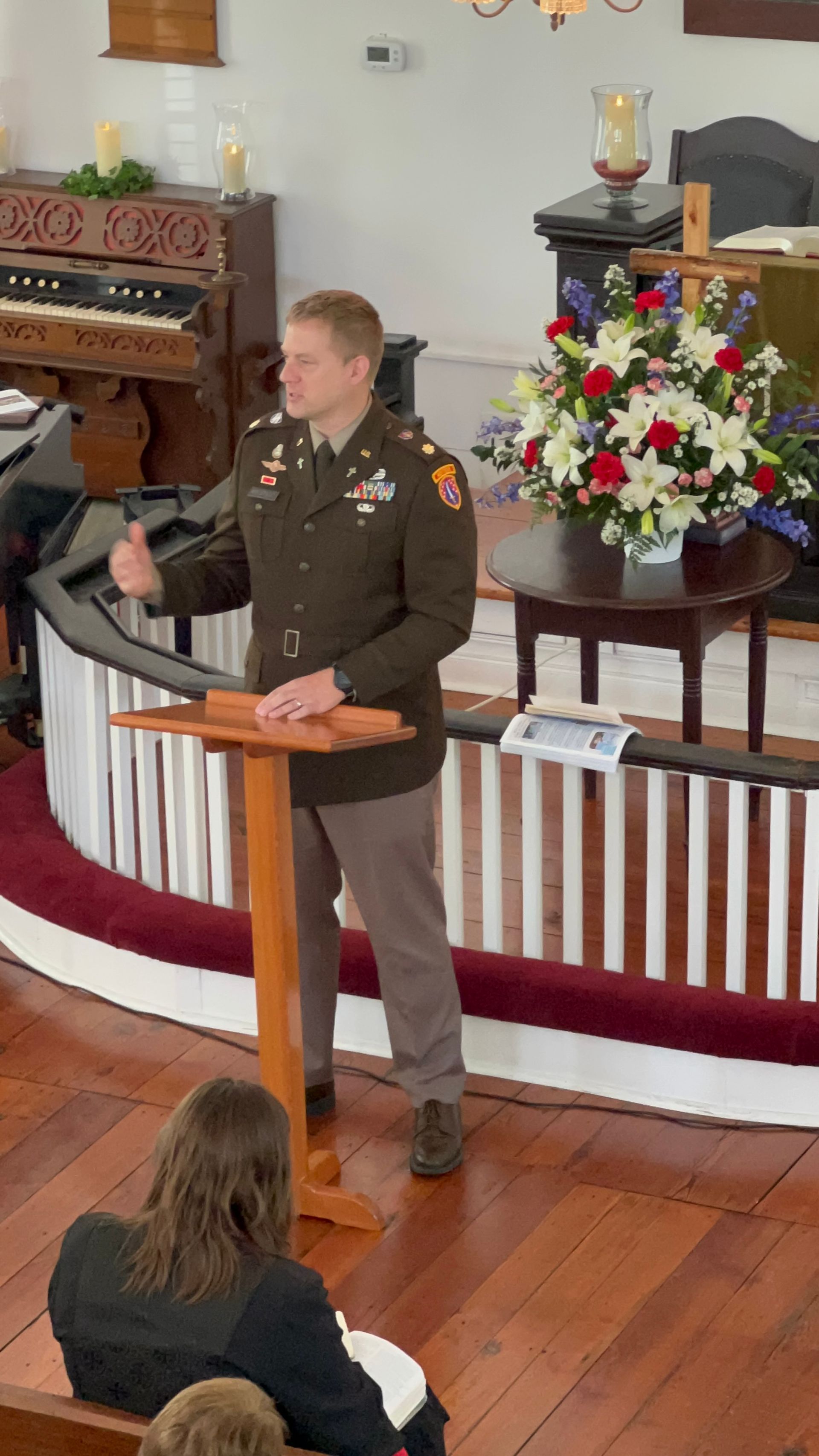 Man in military uniform speaking at a podium in a church. He gestures with his hand.
