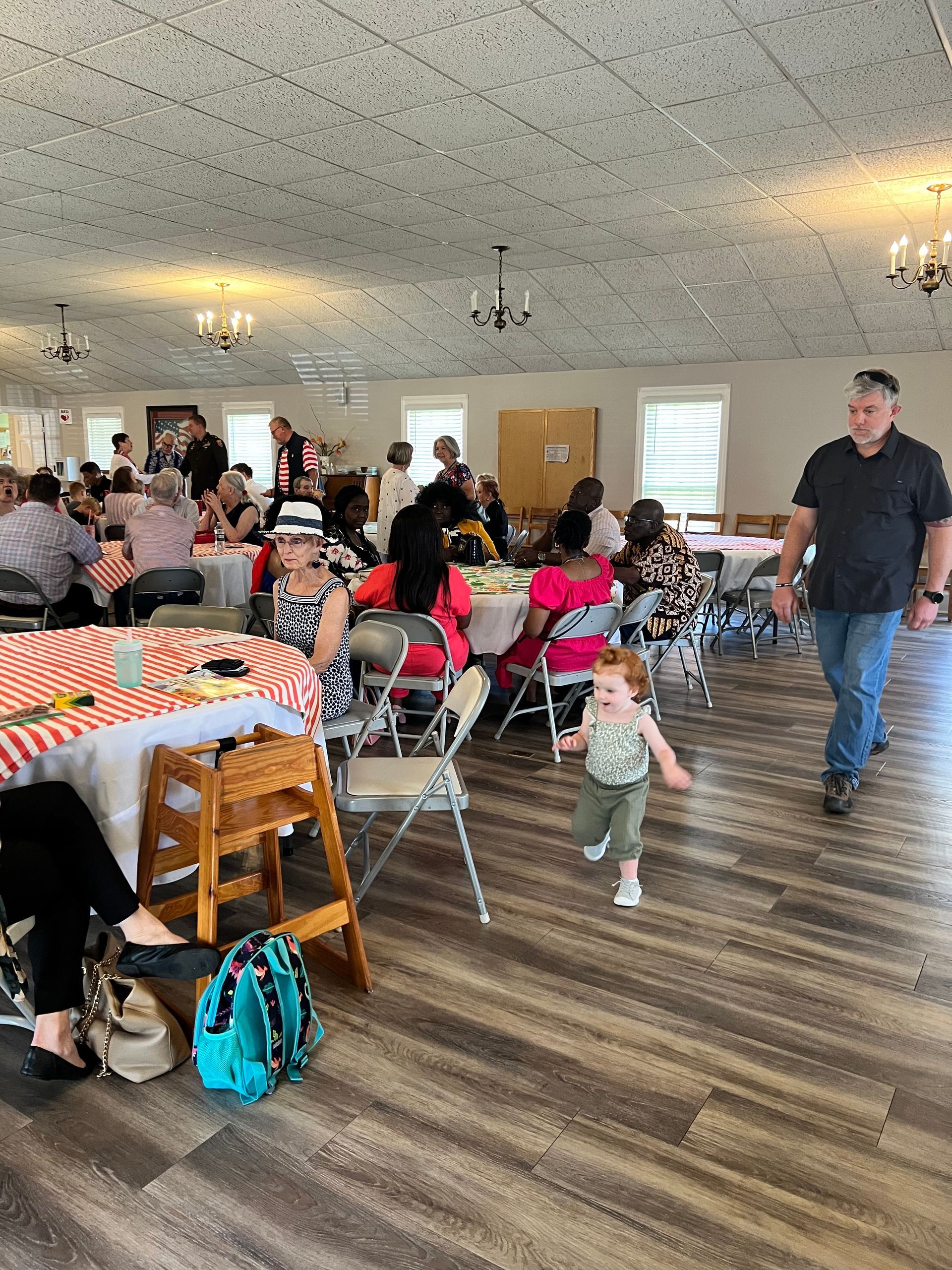 People at a party in a large hall. A child runs towards the camera as a man walks past.