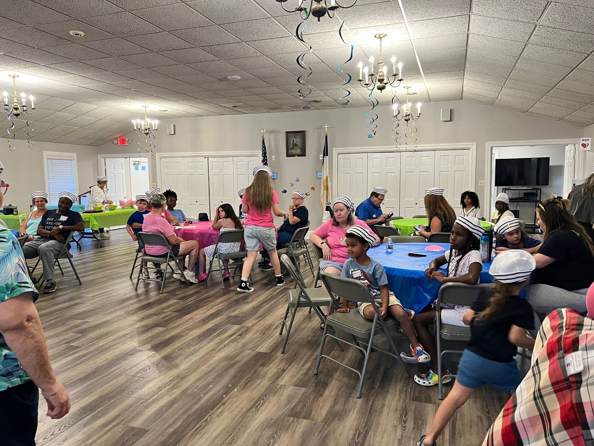 People wearing party hats at tables in a decorated room with balloons and confetti.