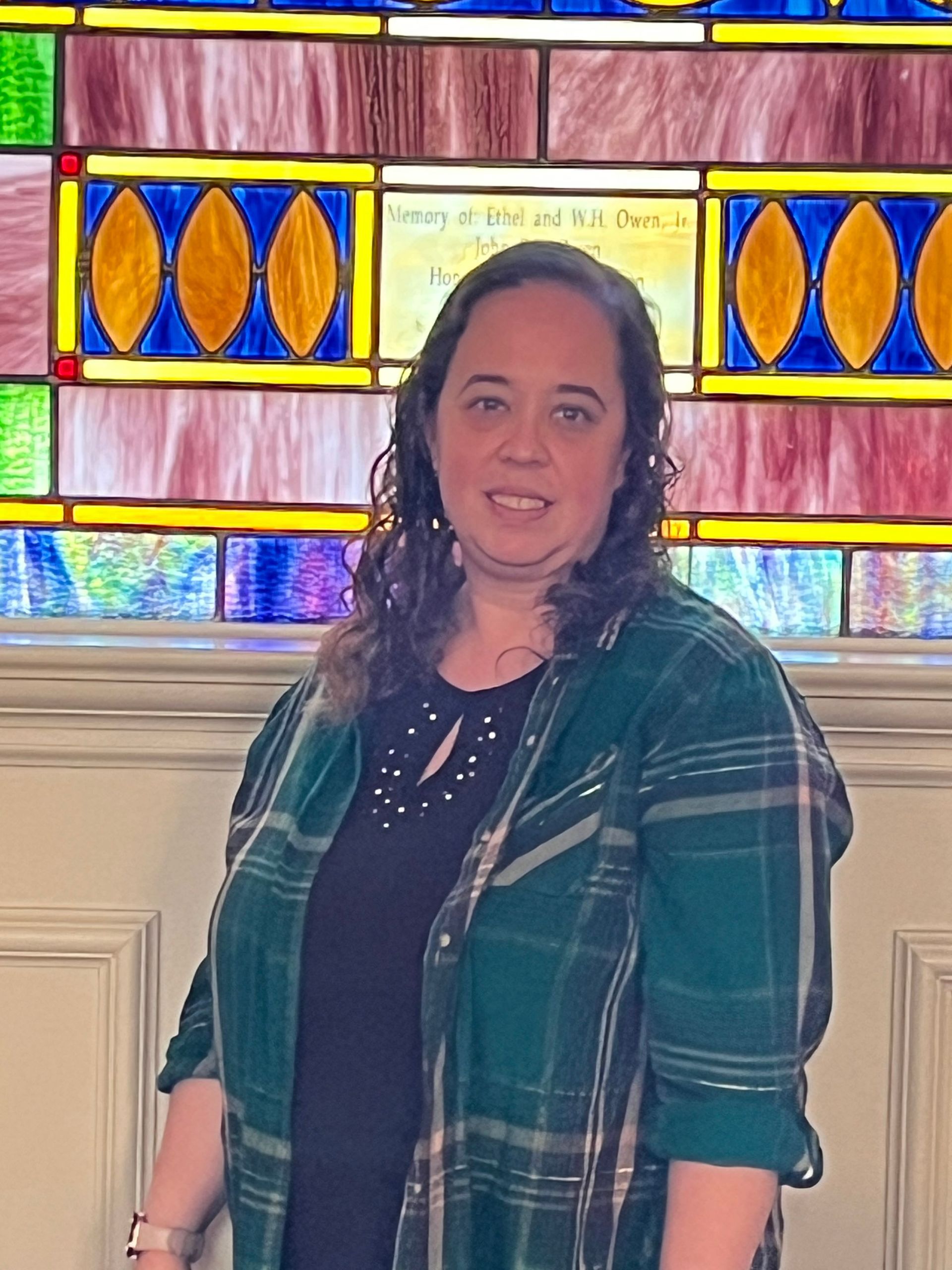 A woman in a plaid shirt is standing in front of a stained glass window.